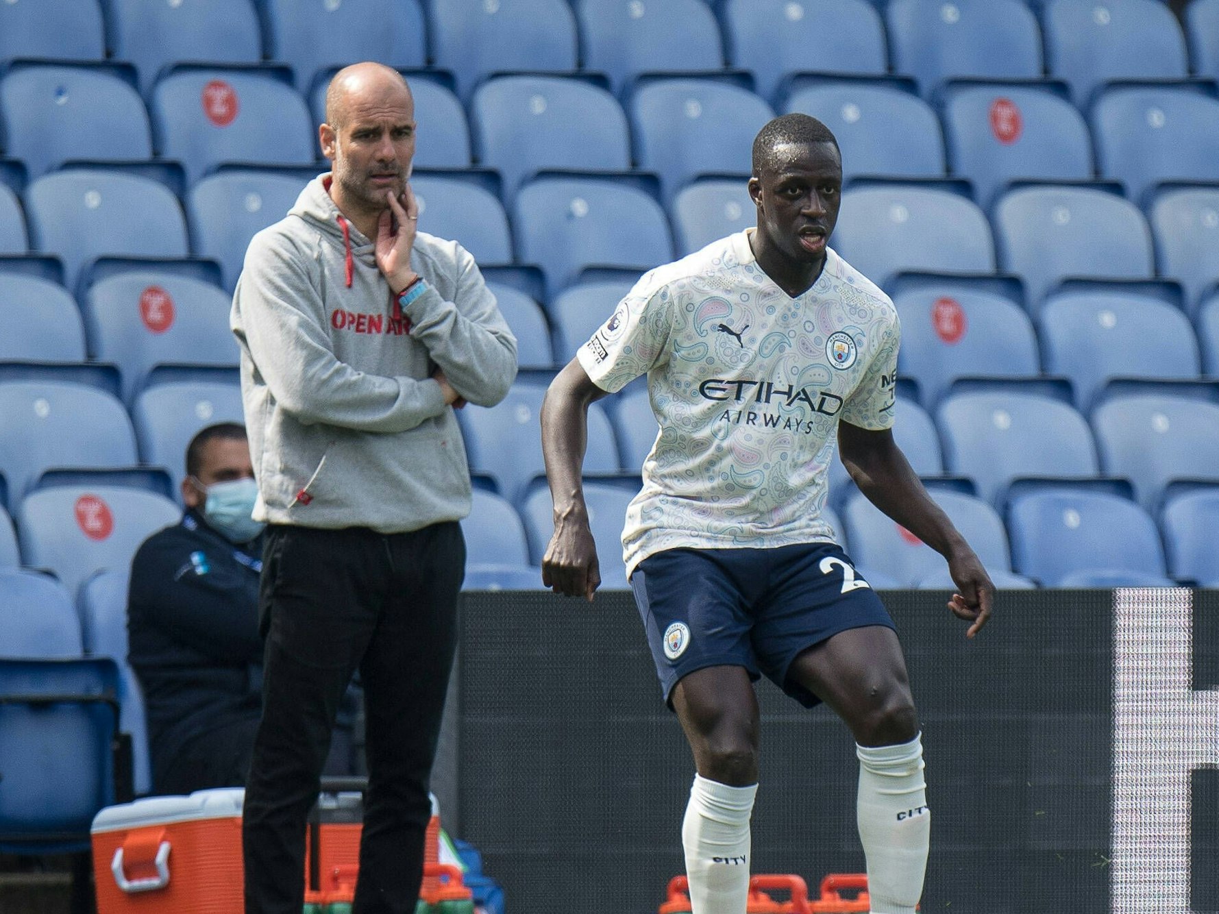 Benjamin Mendy steht auf dem Platz, Pep Guardiola schaut ihm zu.