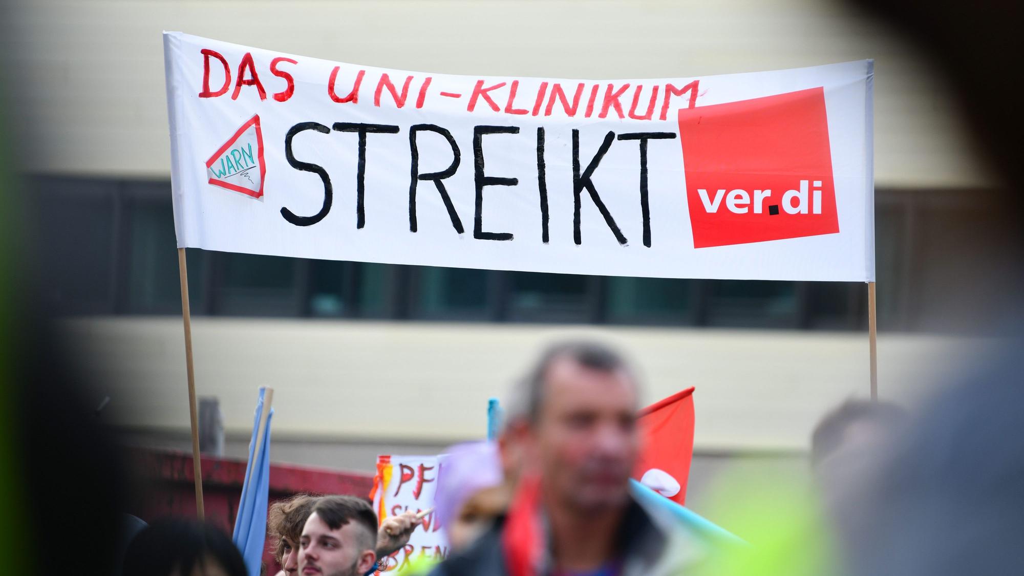 Streikende Beschäftigte halten ein Transparent mit der Aufschrift „Das Uni-Klinikum streikt“ in die Höhe