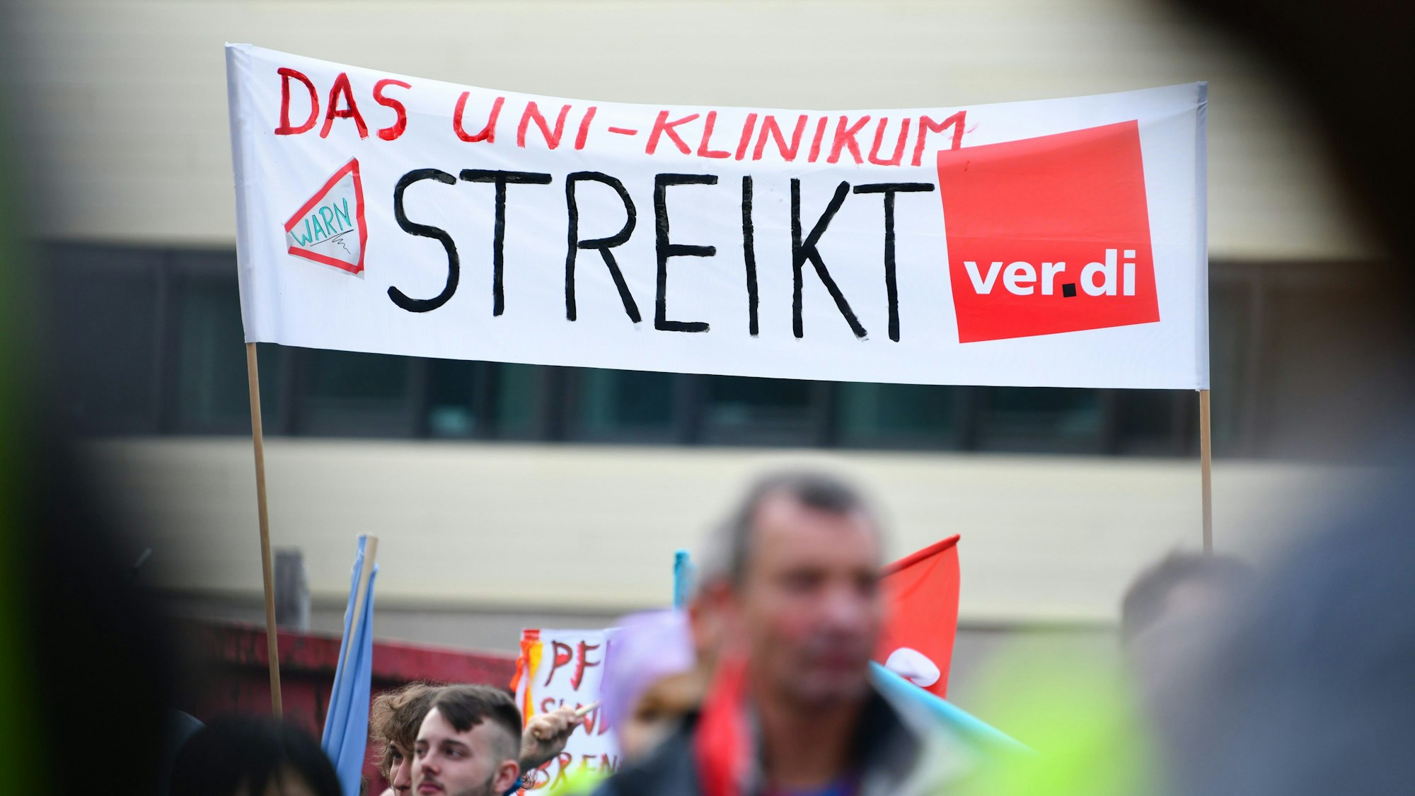 Streikende Beschäftigte halten ein Transparent mit der Aufschrift „Das Uni-Klinikum streikt“ in die Höhe