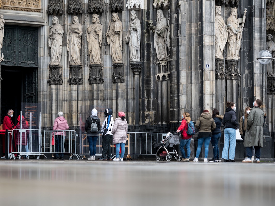 Besucher stehen vor dem Kölner Dom Haupteingang an, am Eingang steht ein sogenannter Domschweizer, eine Aufsichtsperson, aufgenommen am 13. März 2021.