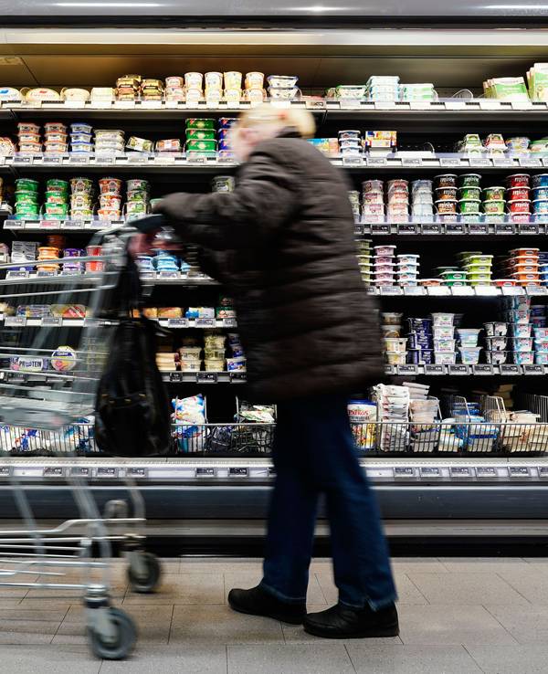 Eine Kundin fährt in einem Supermarkt mit einem Einkaufswagen an einem Lebensmittelregal vorbei.