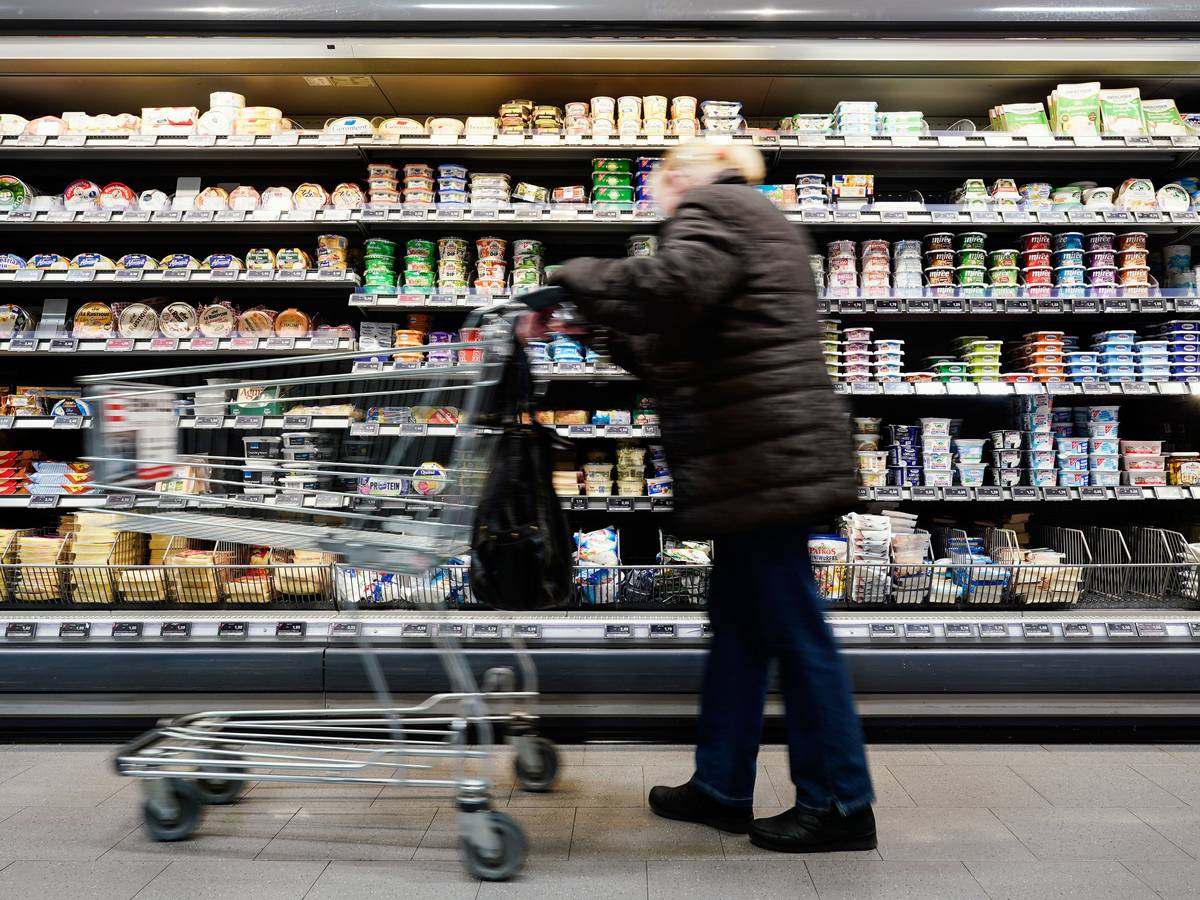 Eine Kundin fährt in einem Supermarkt mit einem Einkaufswagen an einem Lebensmittelregal vorbei.