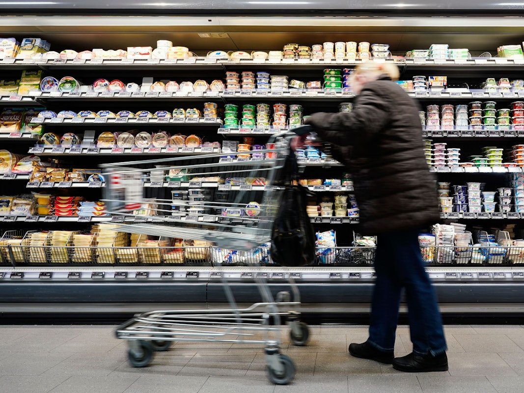 Eine Kundin fährt in einem Supermarkt mit einem Einkaufswagen an einem Lebensmittelregal vorbei.