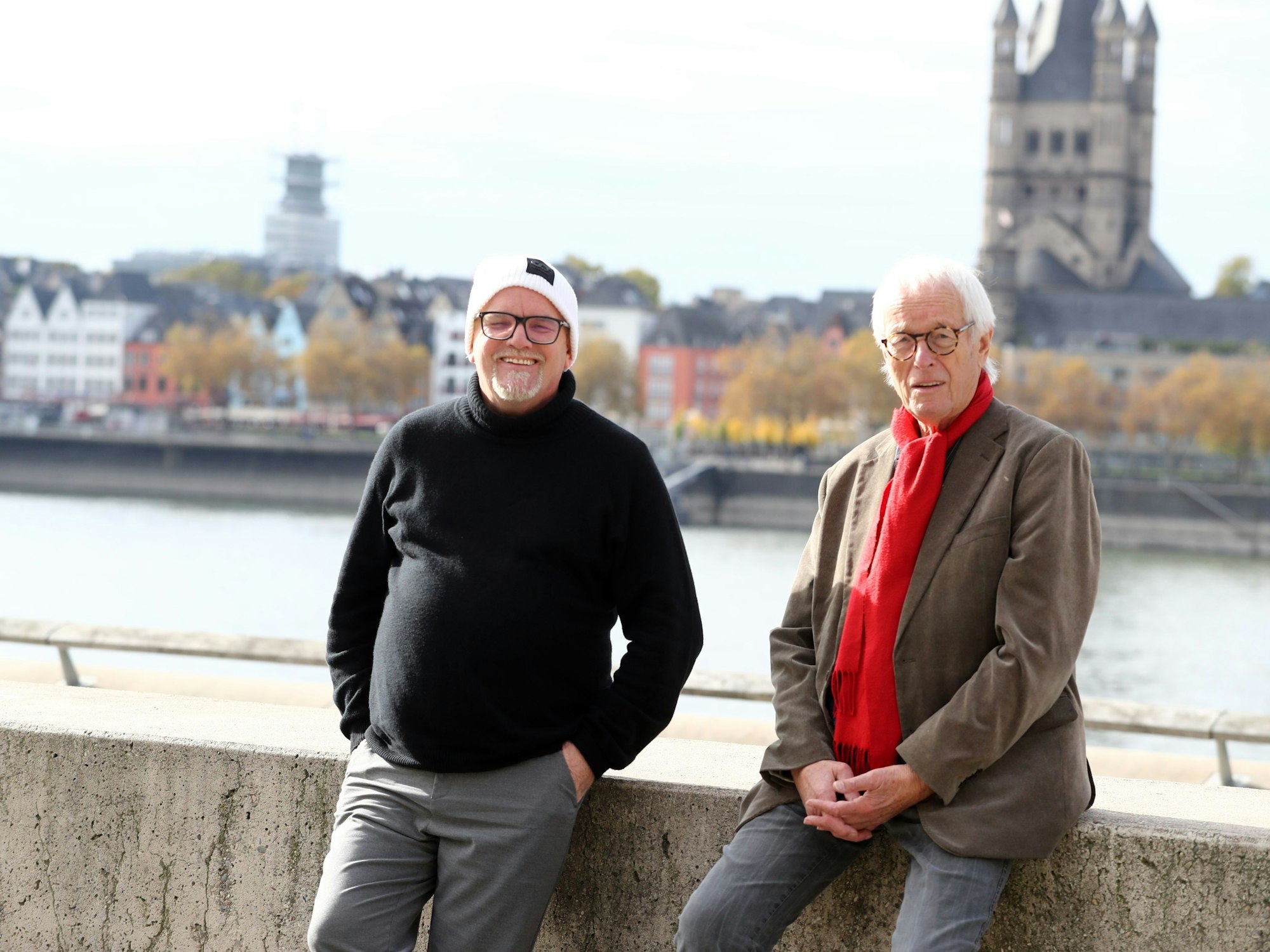 DJ Ötzi (l.) und Reporter Horst Stellmacher sitzen am Rhein und blicken in die Kamera.