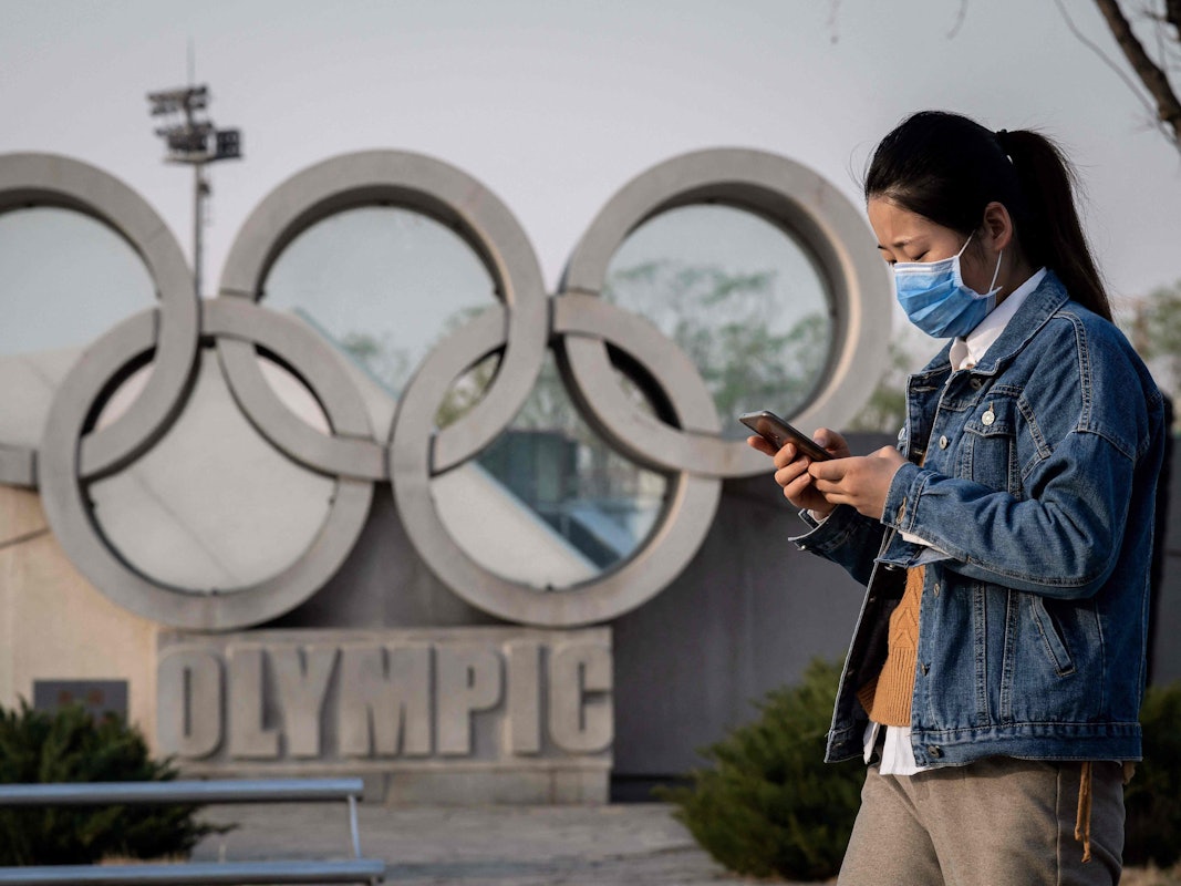 Eine asiatische Frau läuft an der Skulptur der Olympischen Ringe vor dem Nationalstadion „Vogelnest“ in Peking vorbei