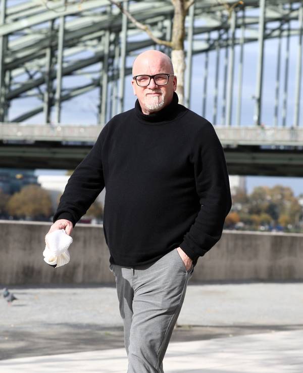 DJ Ötzi läuft am Rhein entlang und blickt in die Kamera.