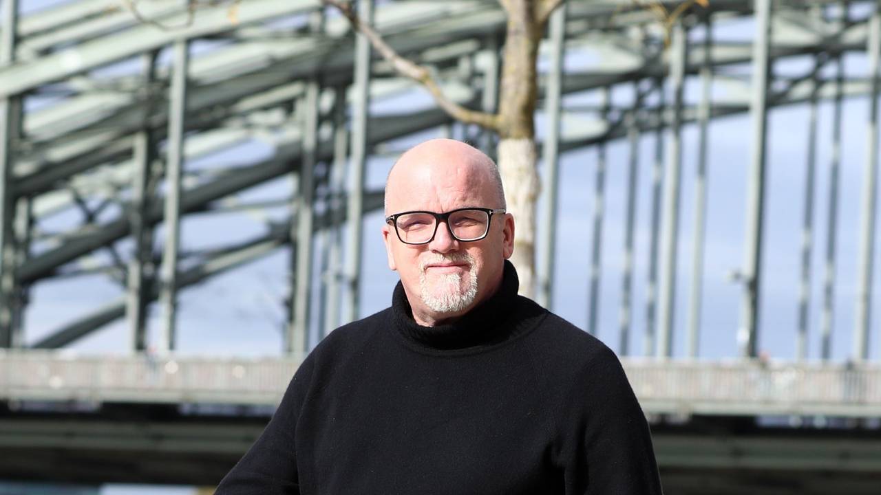 DJ Ötzi läuft am Rhein entlang und blickt in die Kamera.