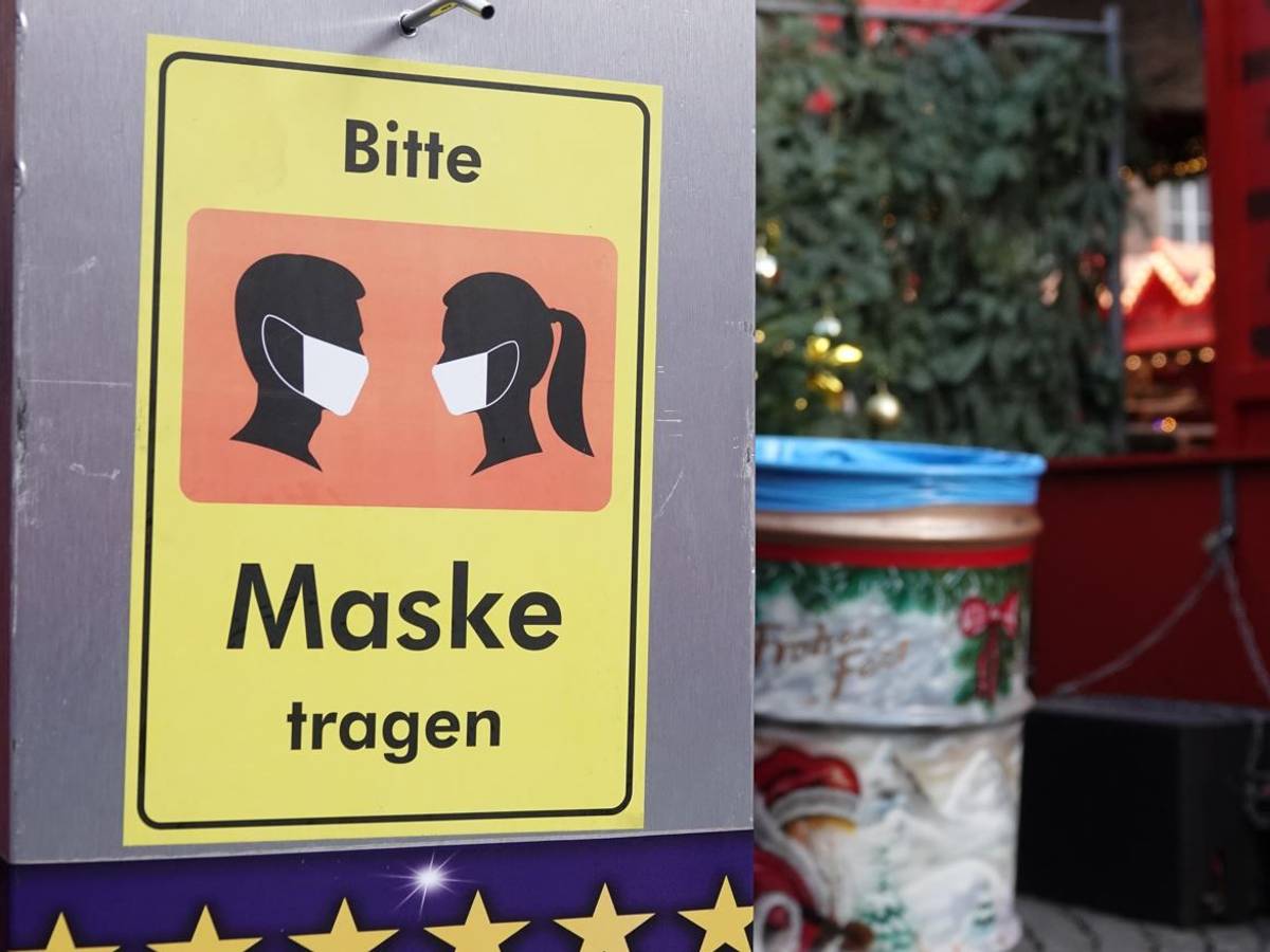 Auf einem Desinfektionsmittelspender am Düsseldorfer Weihnachtsmarkt hängt ein Schild mit der Aufschrift «Bitte Maske tragen».