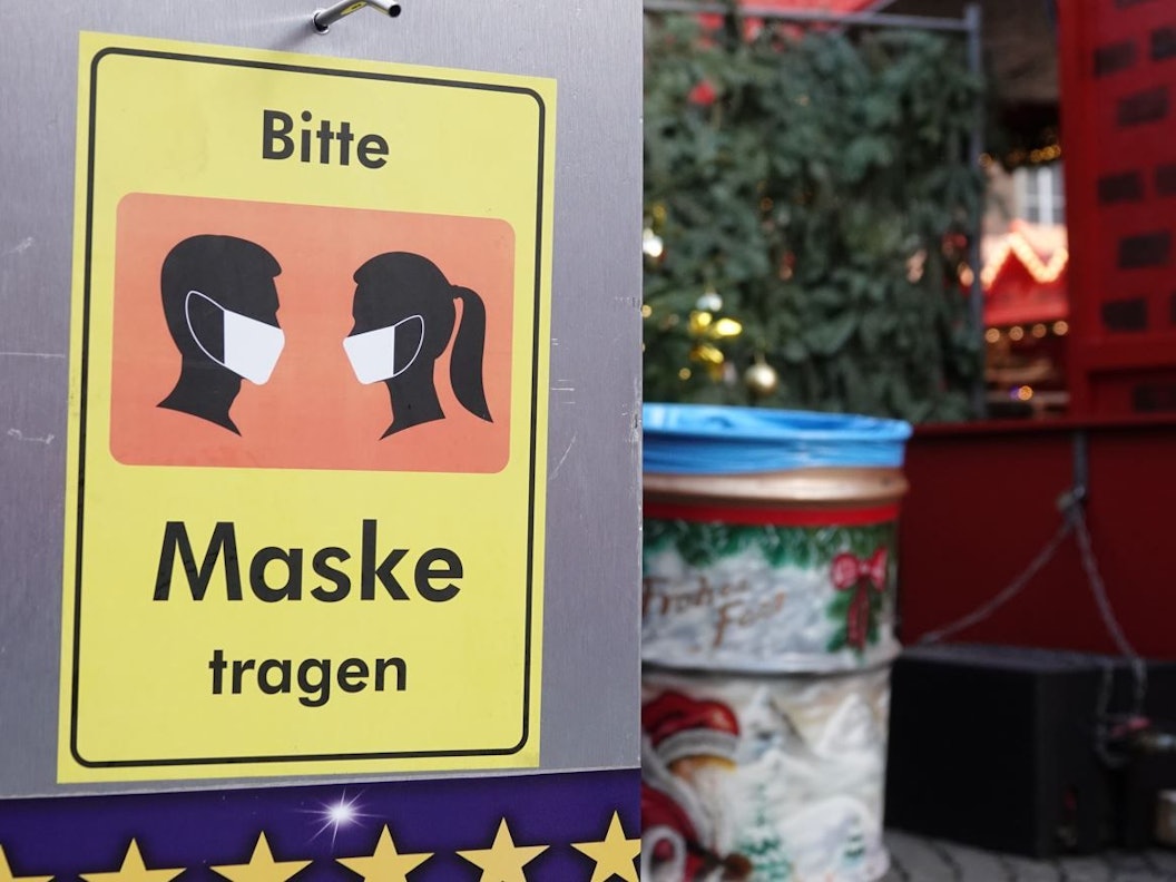 Auf einem Desinfektionsmittelspender am Düsseldorfer Weihnachtsmarkt hängt ein Schild mit der Aufschrift «Bitte Maske tragen».