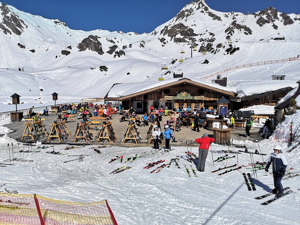 Skifahrer sitzen in Österreich während einer Pause auf der Terrasse einer geschlossenen Skihütte unter Berücksichtigung eines coronabedingten Mindestabstands.