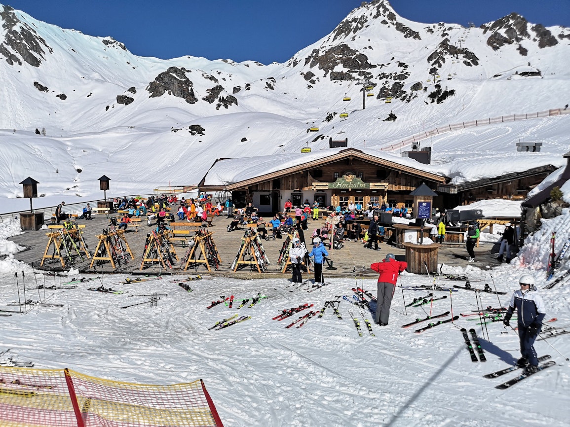 Skifahrer sitzen in Österreich während einer Pause auf der Terrasse einer geschlossenen Skihütte unter Berücksichtigung eines coronabedingten Mindestabstands.