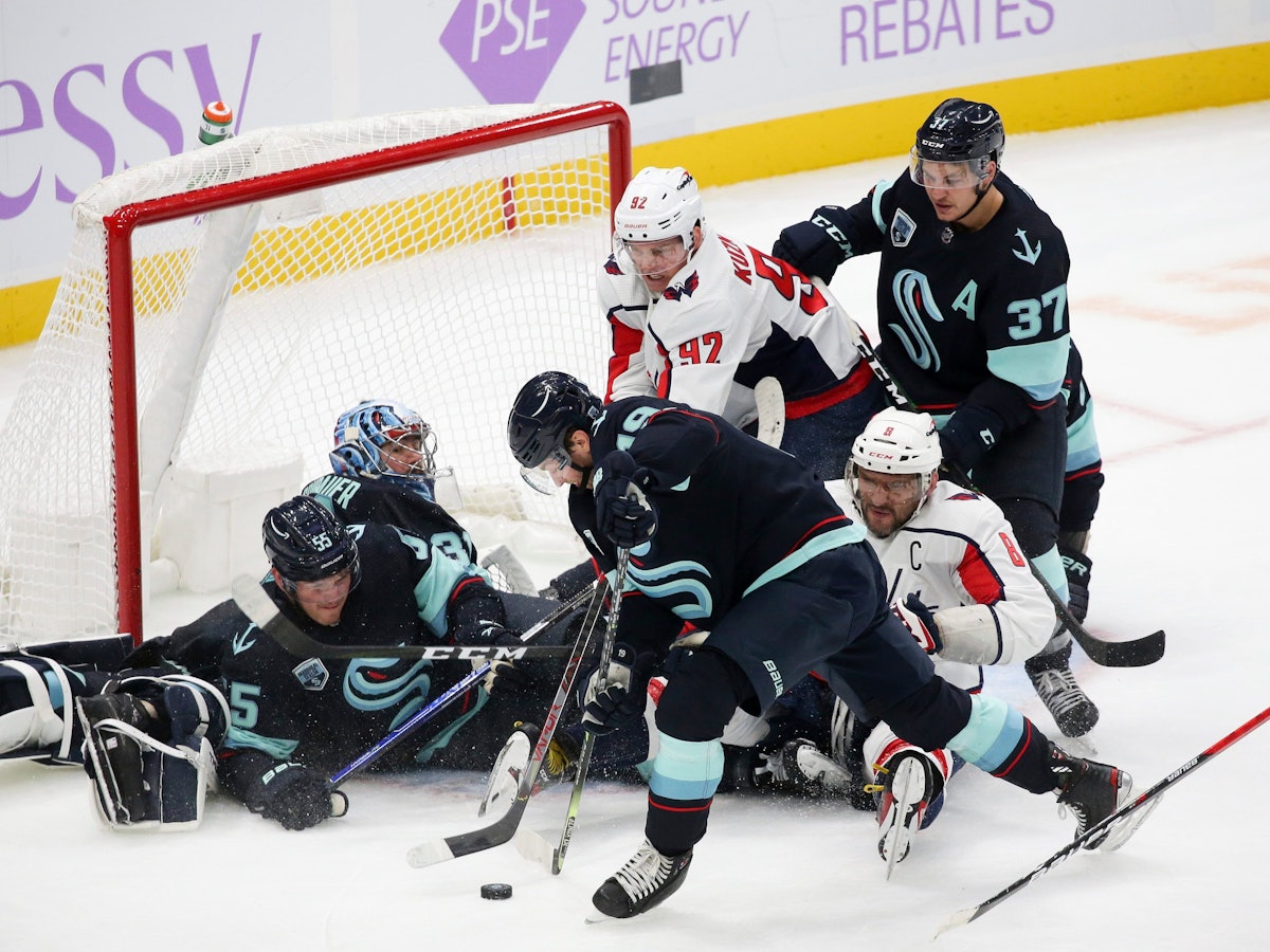 Philipp Grubauer liegt in seinem Tor, weitere Mit- und Gegenspieler tummeln sich um sein Gehäuse. Ein Verteidiger ist im Begriff, den Puck wegzuschlagen.