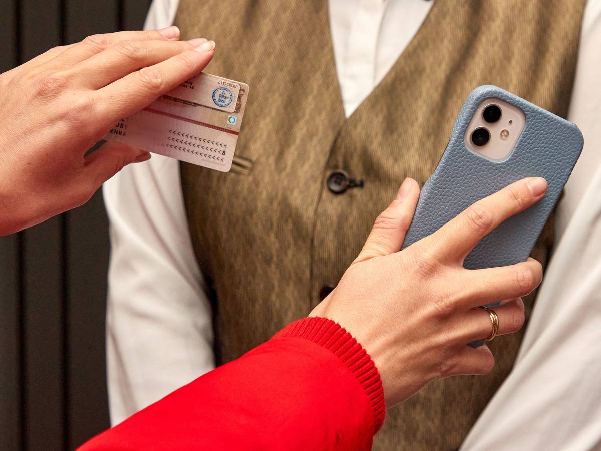 Eine Kinobesucherin (links) hält am 15. November 2021 im Eingang bei der 2G-Kontrolle im Astor Film Lounge HafenCity einer Mitarbeiterin ihren Ausweis und ihr Handy hin.