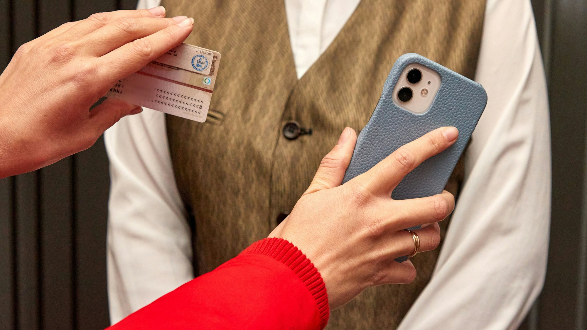 Eine Kinobesucherin (links) hält am 15. November 2021 im Eingang bei der 2G-Kontrolle im Astor Film Lounge HafenCity einer Mitarbeiterin ihren Ausweis und ihr Handy hin.