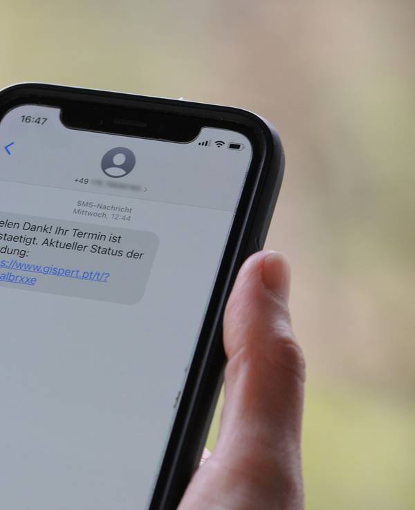 Das Symbolfoto (aufgenommen am 12. April 2021) zeigt eine Frau, die ein Smartphone in ihrer Hand hält, auf dessen Display eine Betrugs-SMS zu lesen ist.