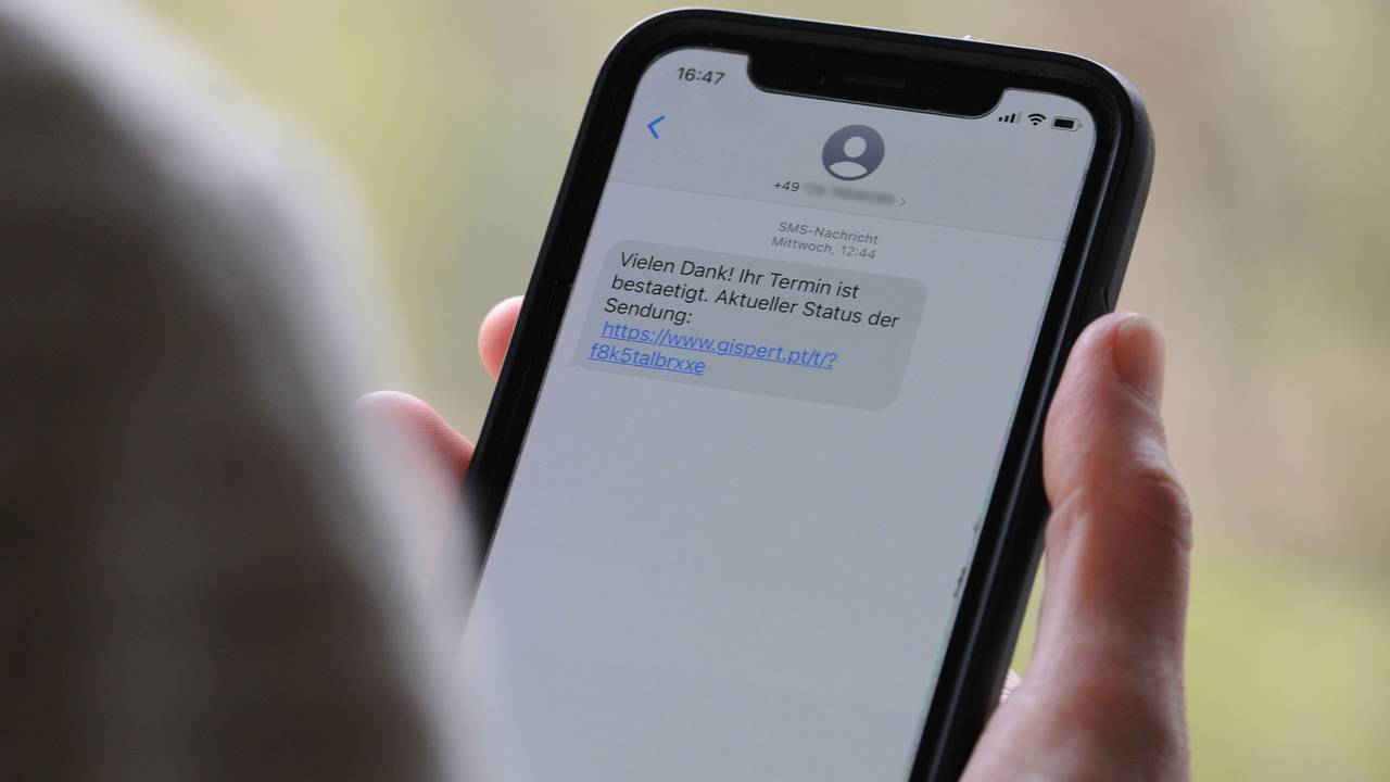 Das Symbolfoto (aufgenommen am 12. April 2021) zeigt eine Frau, die ein Smartphone in ihrer Hand hält, auf dessen Display eine Betrugs-SMS zu lesen ist.