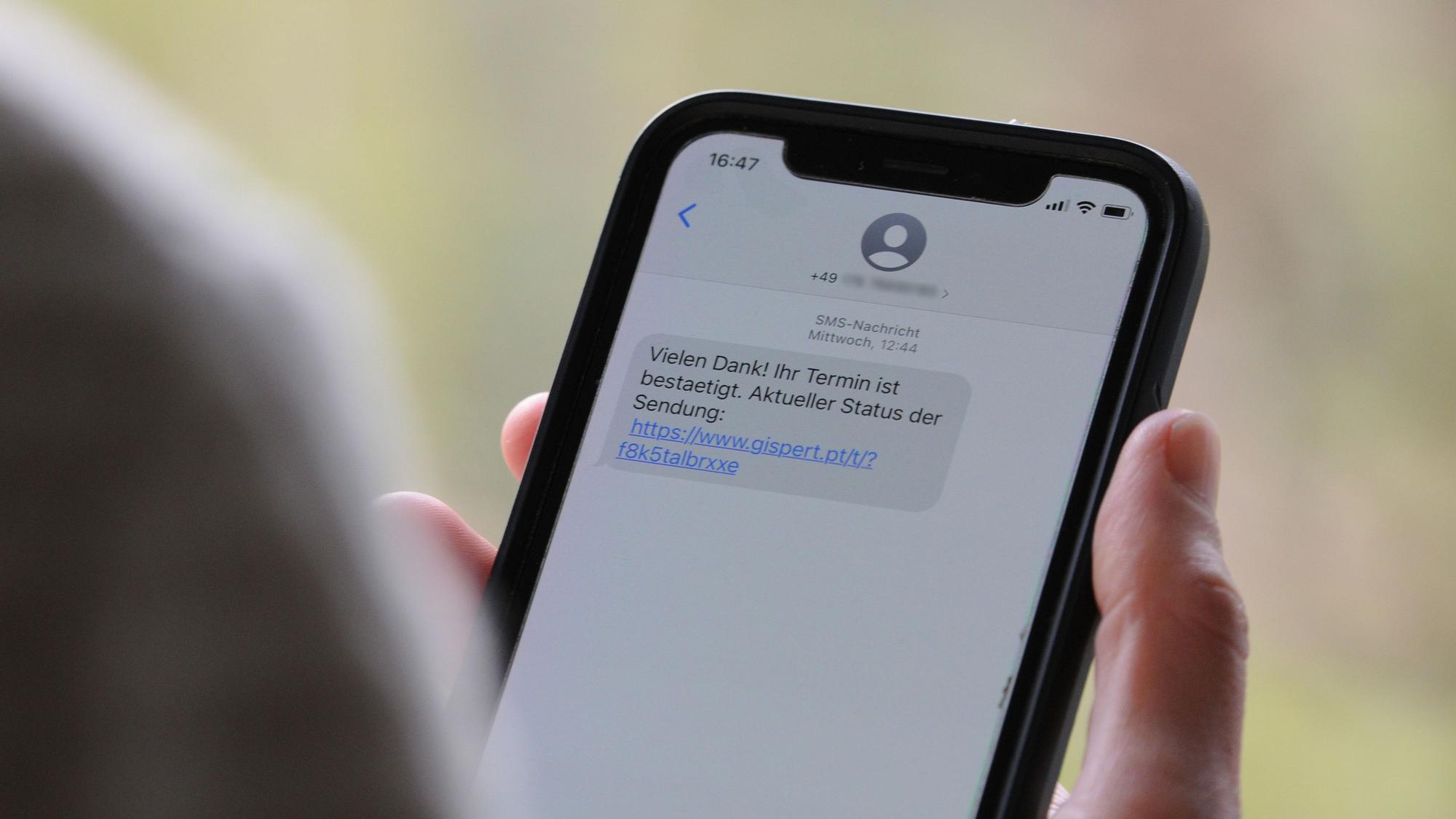 Das Symbolfoto (aufgenommen am 12. April 2021) zeigt eine Frau, die ein Smartphone in ihrer Hand hält, auf dessen Display eine Betrugs-SMS zu lesen ist.