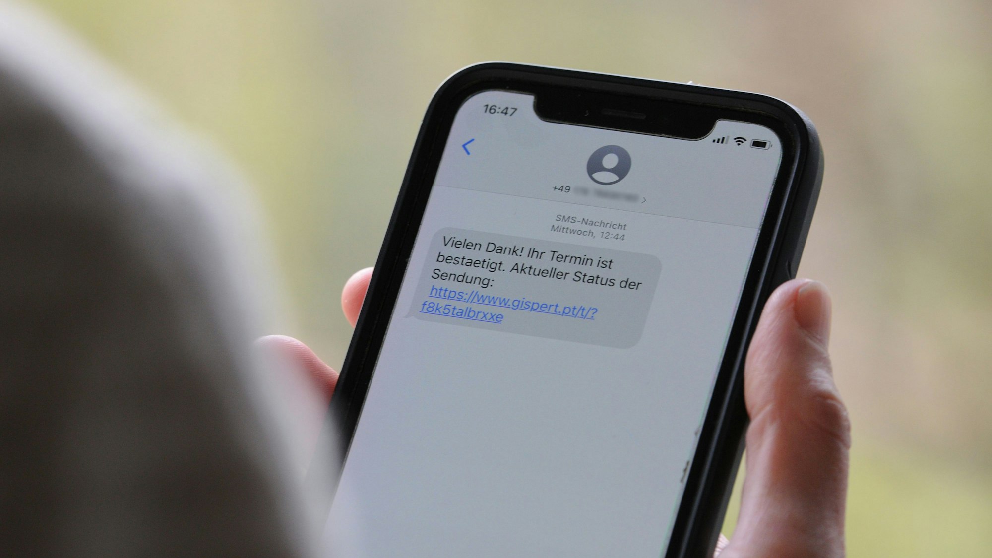 Das Symbolfoto (aufgenommen am 12. April 2021) zeigt eine Frau, die ein Smartphone in ihrer Hand hält, auf dessen Display eine Betrugs-SMS zu lesen ist.
