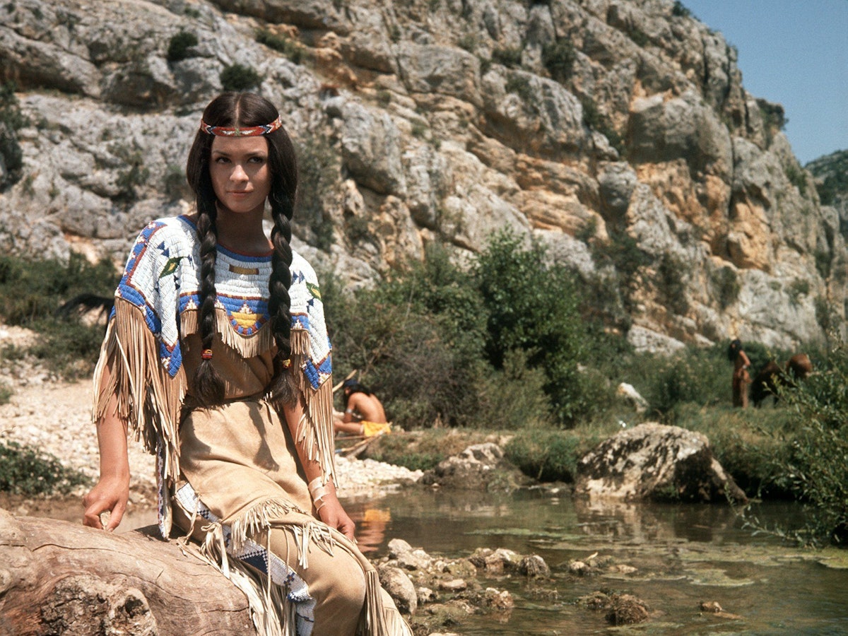 Die französische Schauspielerin Marie Versini in der Rolle von „Winnetous“ Schwester „Nscho-tschi“ in der Verfilmung des ersten „Winnetou“-Romans von Karl May im Jahr 1963 auf einem Stein sitzend.