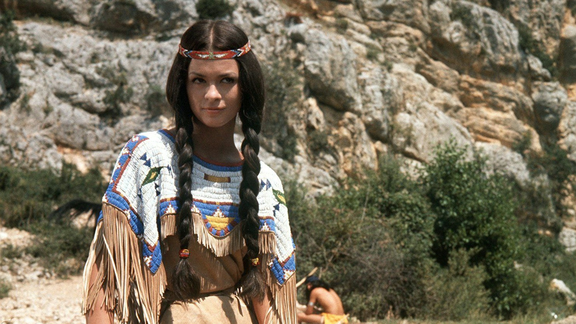Die französische Schauspielerin Marie Versini in der Rolle von „Winnetous“ Schwester „Nscho-tschi“ in der Verfilmung des ersten „Winnetou“-Romans von Karl May im Jahr 1963 auf einem Stein sitzend.