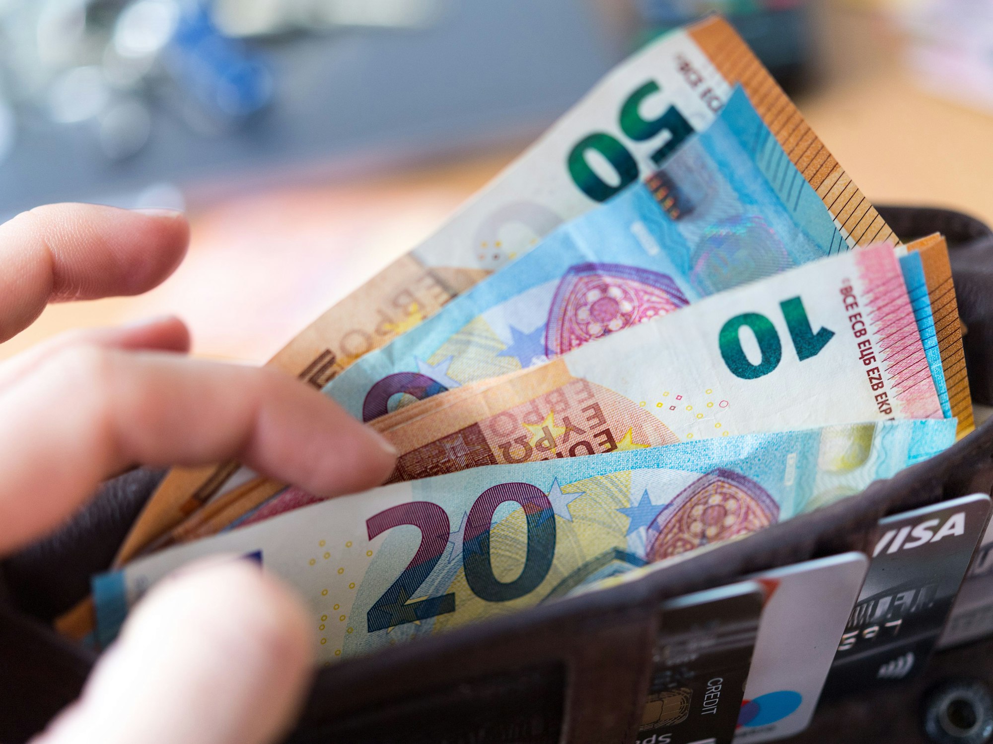 Eine Frau hält eine Geldbörse mit zahlreichen Banknoten und Bankkarten in der Hand.