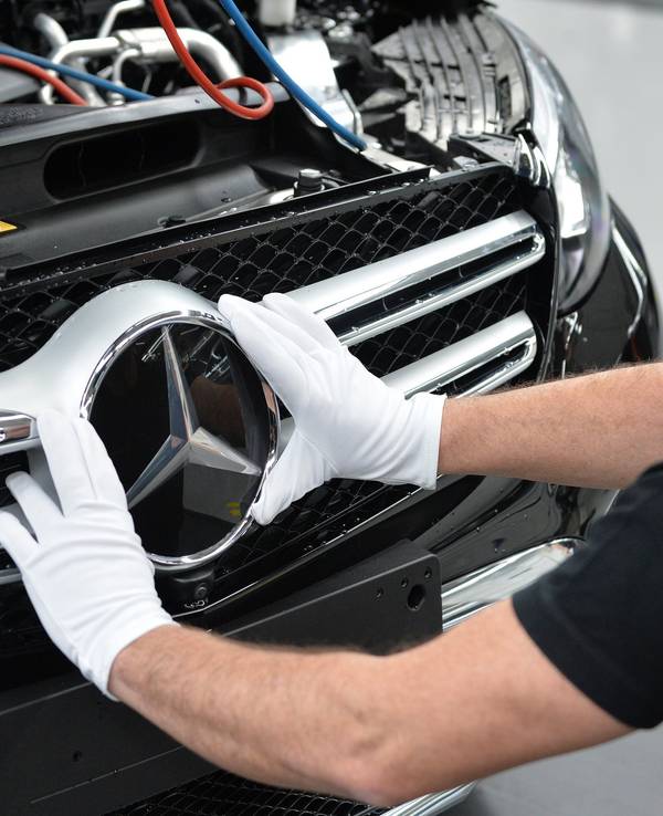 Mercedes-Benz ruft acht Modelle zurück. Dieses undatierte Symbolfoto zeigt einen Arbeiter, der einen Mercedes-Stern am Fahrzeug montiert.