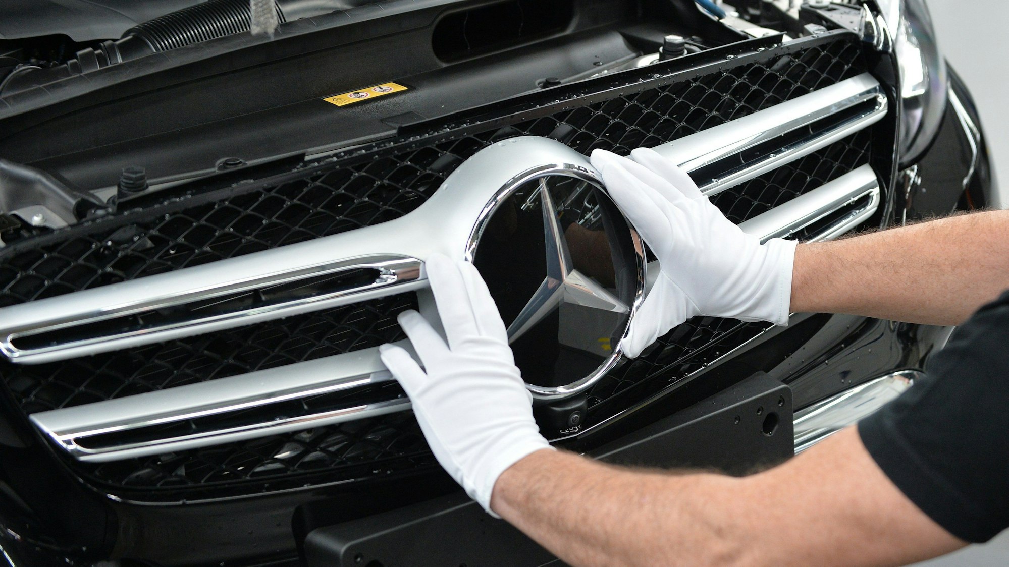 Mercedes-Benz ruft acht Modelle zurück. Dieses undatierte Symbolfoto zeigt einen Arbeiter, der einen Mercedes-Stern am Fahrzeug montiert.