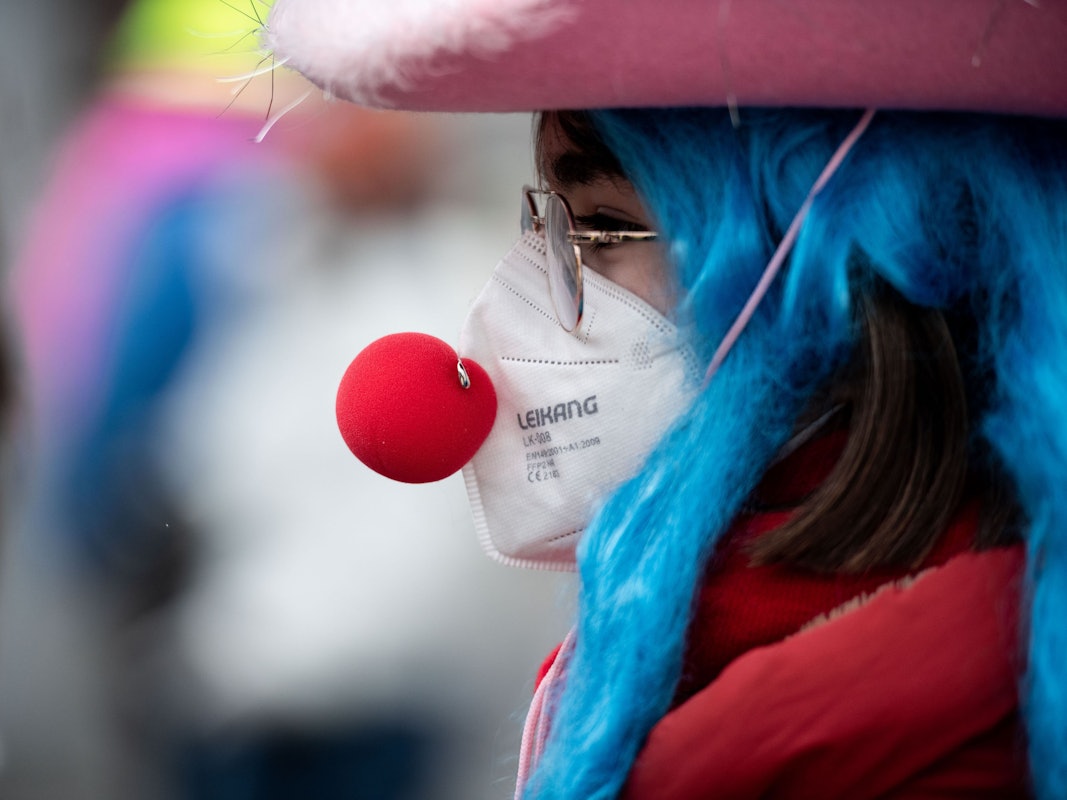 Eine verkleidete Frau trägt eine Clownsnase über einer FFP2 Maske.
