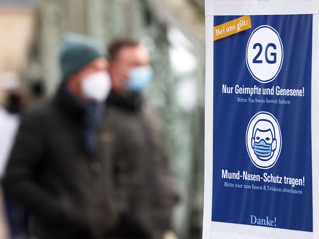 Besucher eines Weihnachtsmarktes in Köln gehen an einem Schild vorbei, das auf die 2G-Regel (Nur Geimpfte und Genesene) hinweist.