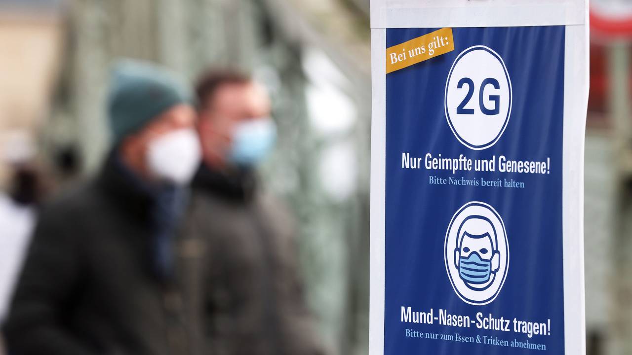 Besucher eines Weihnachtsmarktes in Köln gehen an einem Schild vorbei, das auf die 2G-Regel (Nur Geimpfte und Genesene) hinweist.