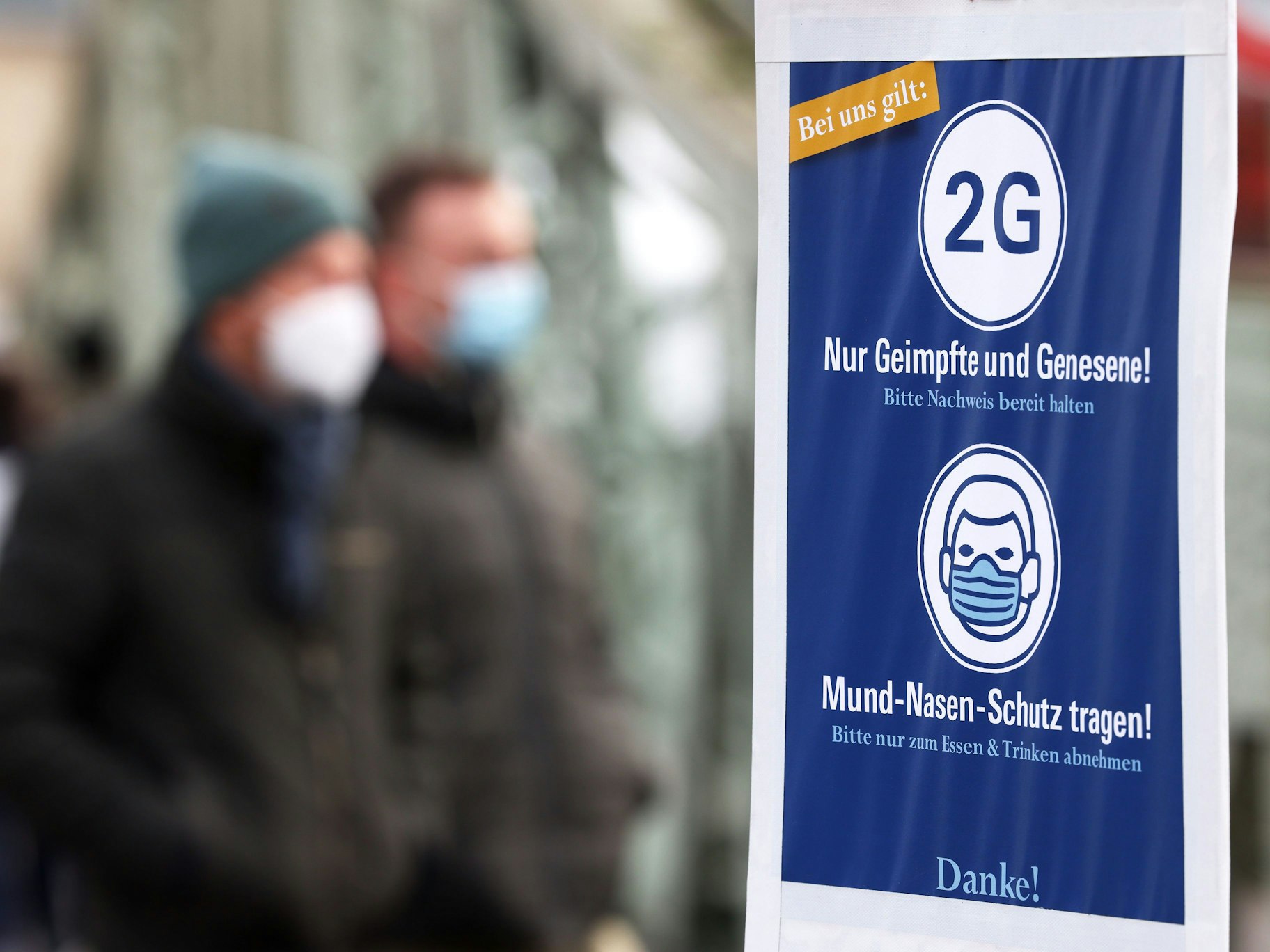 Besucher eines Weihnachtsmarktes in Köln gehen an einem Schild vorbei, das auf die 2G-Regel (Nur Geimpfte und Genesene) hinweist.