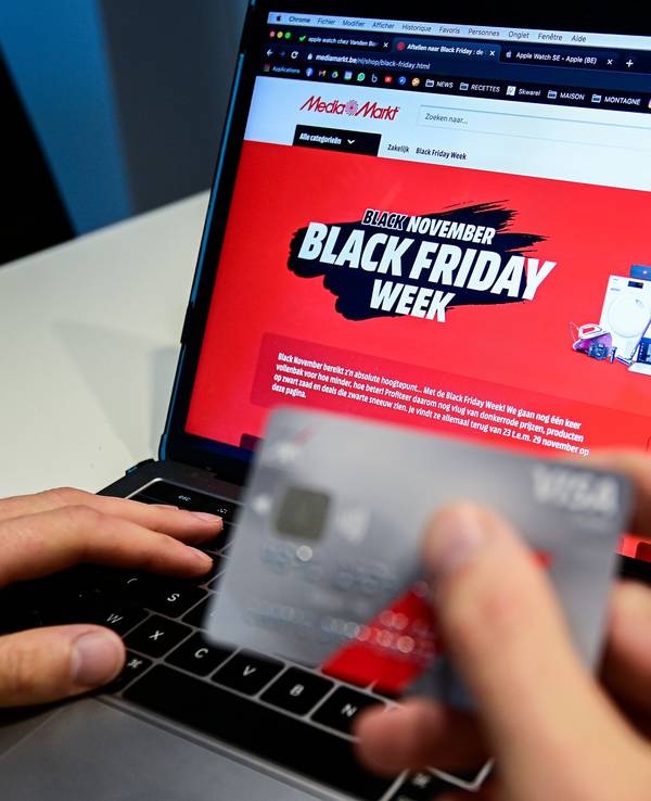 Eine Person hält eine Kreditkarte, während auf einem Laptop zu lesen ist „Black November. Black Friday Woche“.