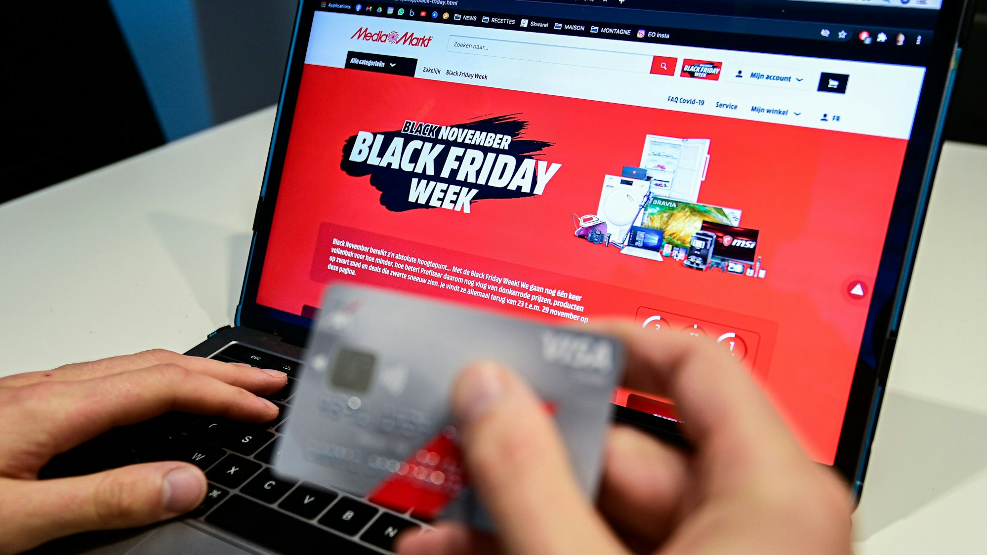 Eine Person hält eine Kreditkarte, während auf einem Laptop zu lesen ist „Black November. Black Friday Woche“.
