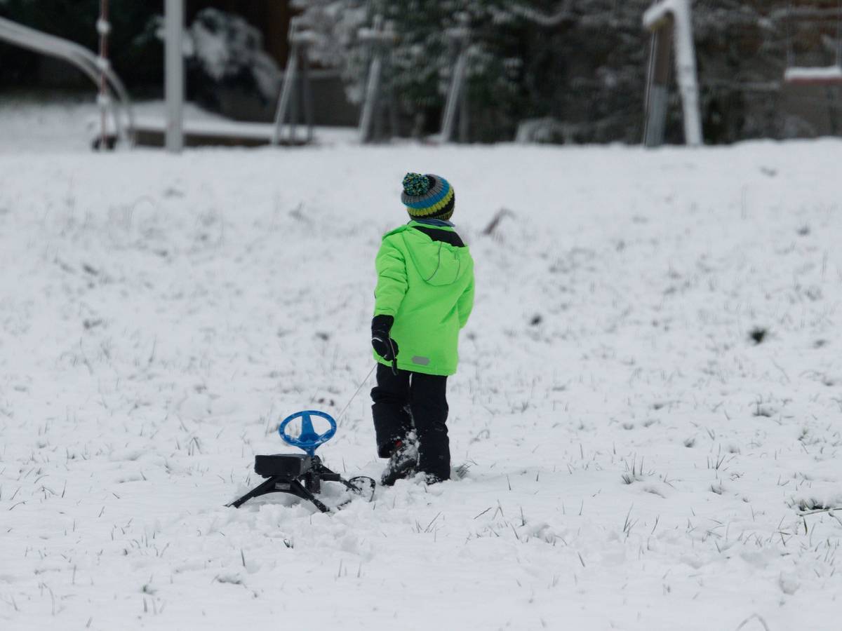Ein Kind zieht neben der Skipiste Rauher Busch einen Schlitten über den Schnee.