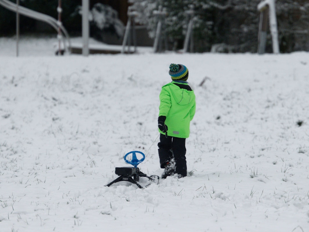 Ein Kind zieht neben der Skipiste Rauher Busch einen Schlitten über den Schnee.