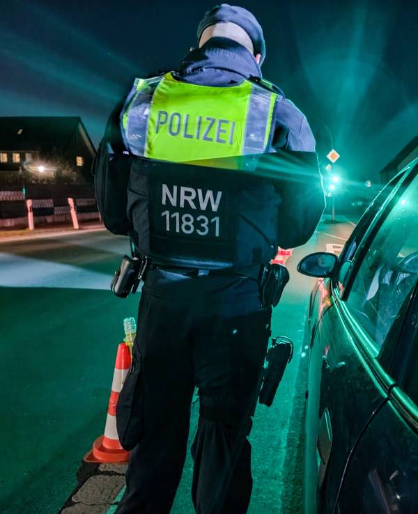 Ein Polizist steht an einem Auto und führt eine Kontrolle durch.