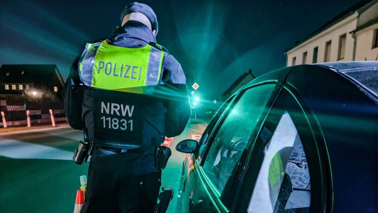 Ein Polizist steht an einem Auto und führt eine Kontrolle durch.