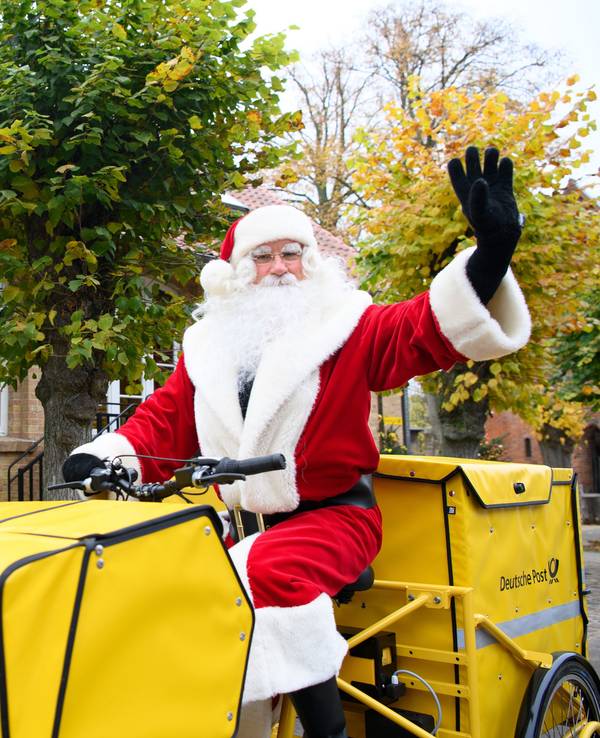 Der Weihnachtsmann sitzt nach seiner Ankunft am Weihnachtspostamt winkend auf dem Fahrrad.