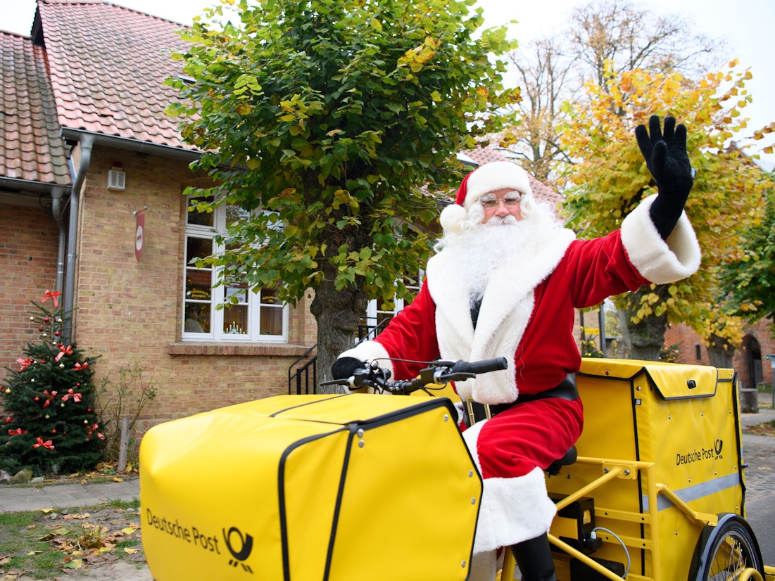 Der Weihnachtsmann sitzt nach seiner Ankunft am Weihnachtspostamt winkend auf dem Fahrrad.