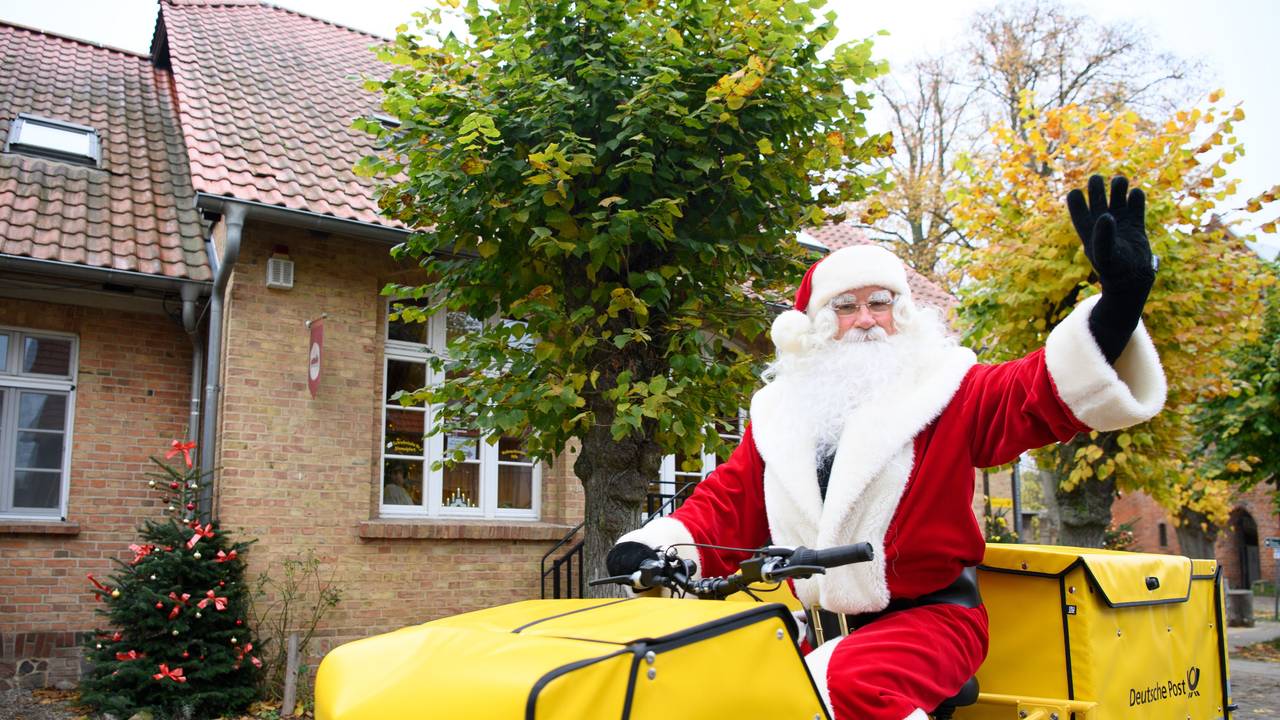 Der Weihnachtsmann sitzt nach seiner Ankunft am Weihnachtspostamt winkend auf dem Fahrrad.