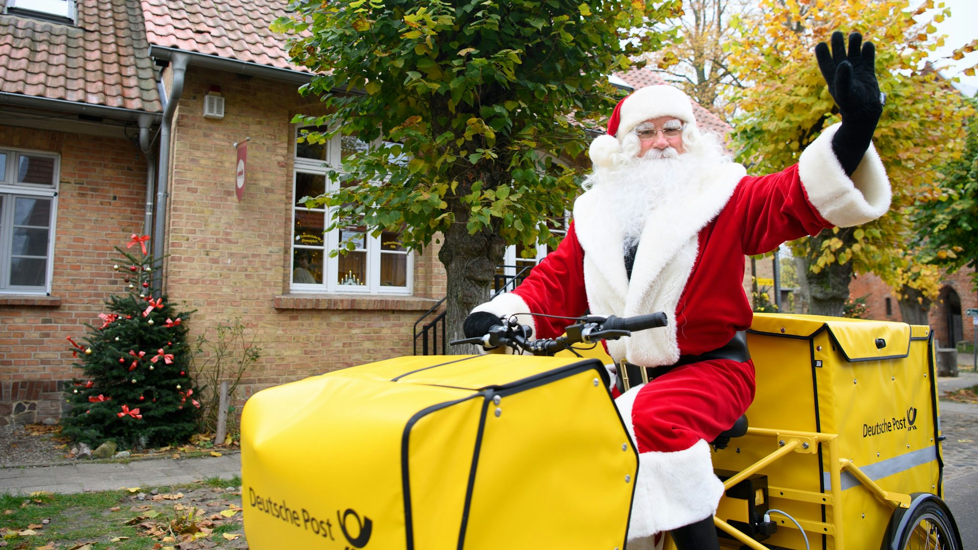 Der Weihnachtsmann sitzt nach seiner Ankunft am Weihnachtspostamt winkend auf dem Fahrrad.