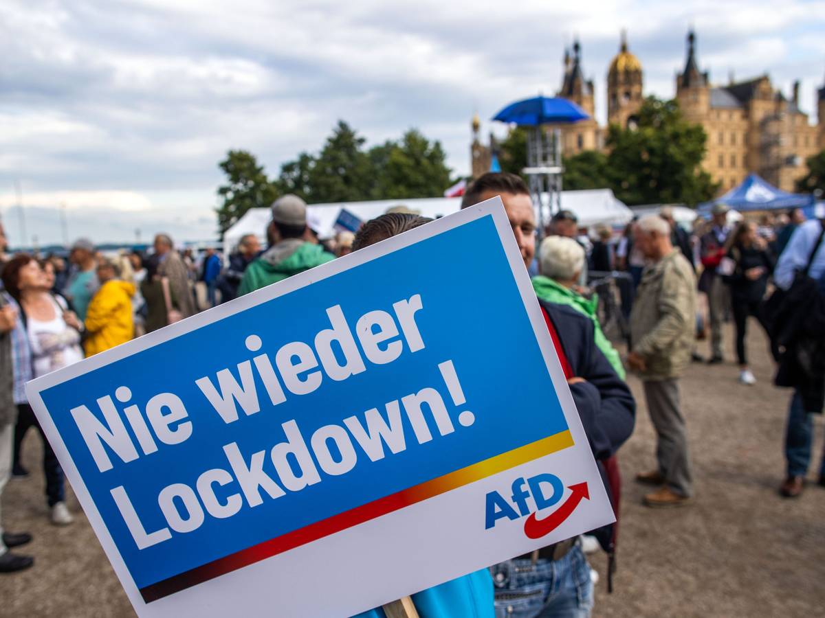 Ein Anhänger der AfD steht mit einem Plakat mit der Aufschrift „Nie wieder Lockdown“ zum Auftakt der Wahlkampftour der AfD vor dem Schweriner Schloss.