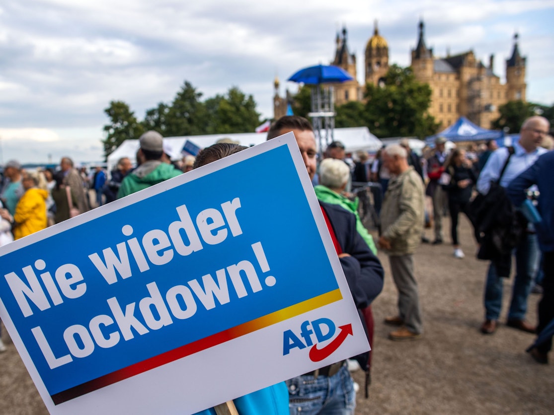 Ein Anhänger der AfD steht mit einem Plakat mit der Aufschrift „Nie wieder Lockdown“ zum Auftakt der Wahlkampftour der AfD vor dem Schweriner Schloss.