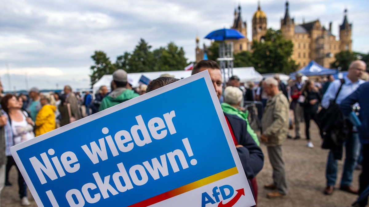 Ein Anhänger der AfD steht mit einem Plakat mit der Aufschrift „Nie wieder Lockdown“ zum Auftakt der Wahlkampftour der AfD vor dem Schweriner Schloss.