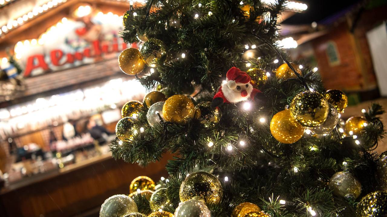 Auf dem Symbolfoto sieht man einen geschmückten Weihnachtsbaum, der vor einem beleuchteten Weihnachtsstand leuchtet.