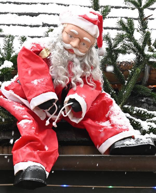 Eine Weihnachtsmannfigur hängt als Dekoration an einem Dach.