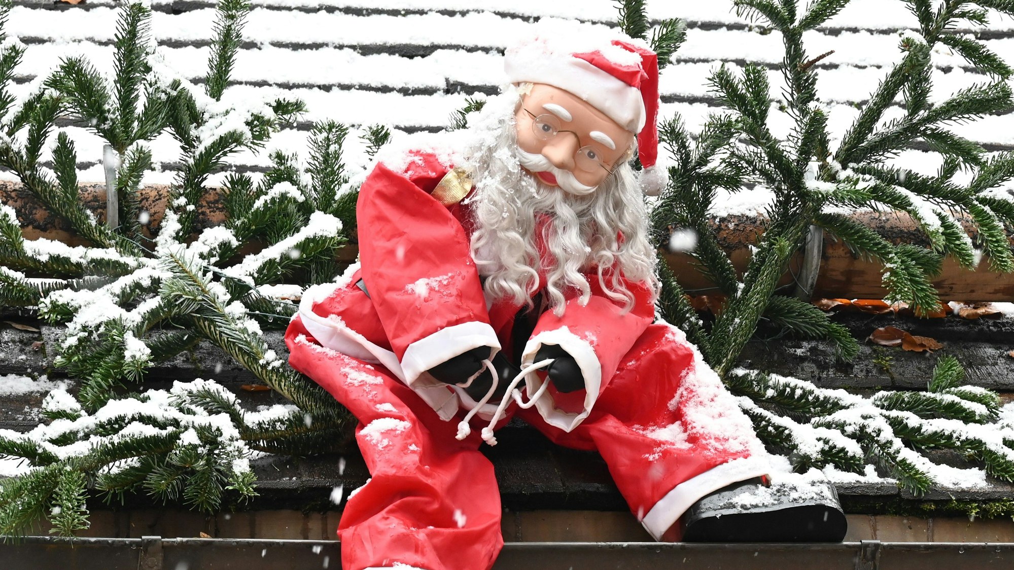 Eine Weihnachtsmannfigur hängt als Dekoration an einem Dach.