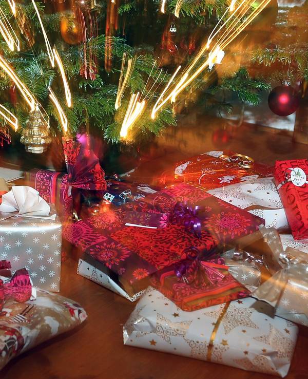 Verpackte Weihnachtsgeschenke liegen unter einem Christbaum.