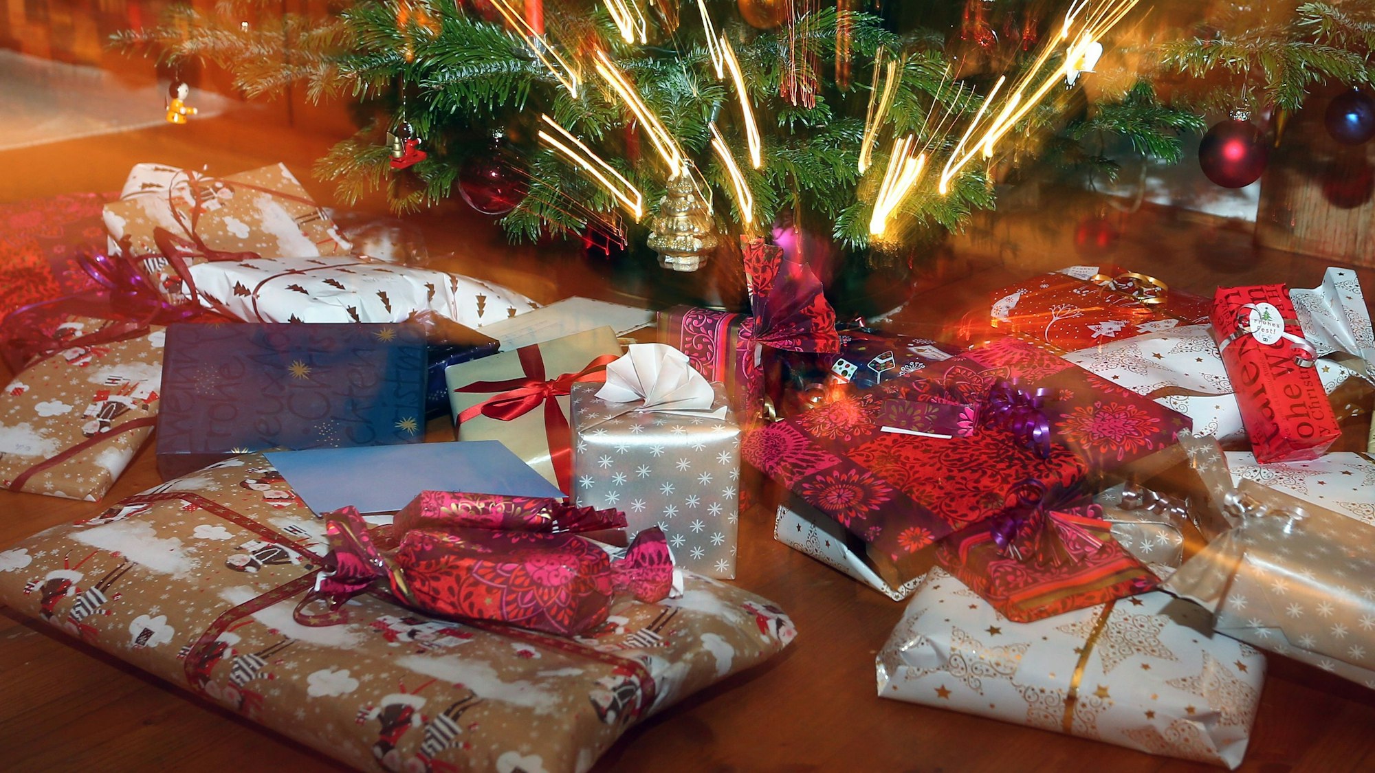 Verpackte Weihnachtsgeschenke liegen unter einem Christbaum.