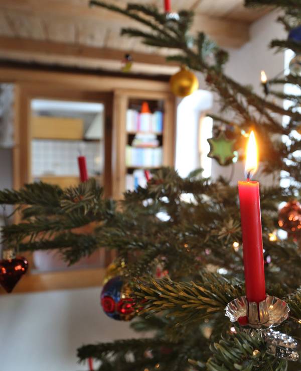 Eine Kerze brennt an einem geschmückten Weihnachtsbaum.